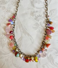 a necklace with lots of different colored beads on a silver chain and an ornate background