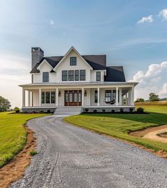 a large white house sitting on top of a lush green field next to a dirt road