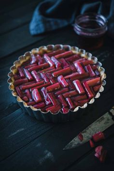 a tart dish filled with sliced strawberries next to a knife and jar of jam