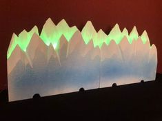 a paper sculpture with green and white lights in the shape of mountains on top of each other