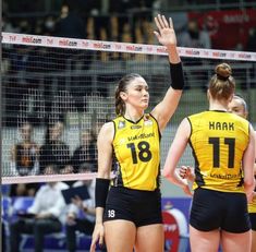 two women in yellow and black volleyball uniforms are high fiving each other over the net