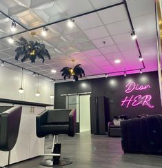 the interior of a hair salon with black chairs and neon lights hanging from the ceiling