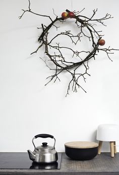 a tea kettle sitting on top of a table next to a tree branch decoration with apples hanging from it