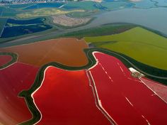 an aerial view of red and green fields from the air, with water in the foreground