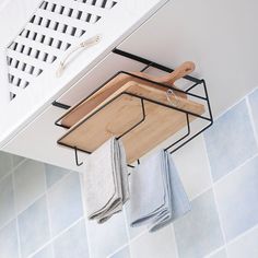 a wooden cutting board hanging from the side of a kitchen cabinet over a towel rack