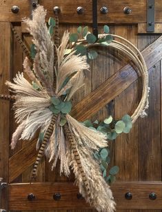 a wreath made out of dried grass and leaves hanging on a wooden door with rivets