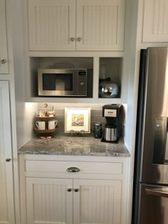 a kitchen with white cabinets and granite counter tops, stainless steel refrigerator and coffee maker