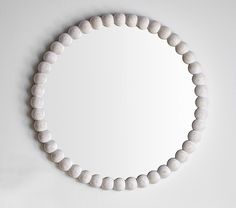 a round mirror mounted on the wall above a white beaded bracelet that is hanging from it's side