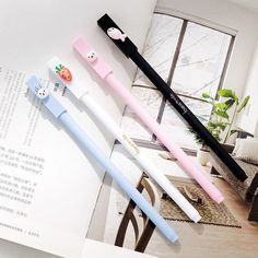 three pens sitting on top of an open book next to each other in front of a window