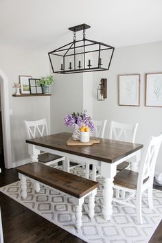 a dining room table with white chairs and a bench in front of it on top of a rug