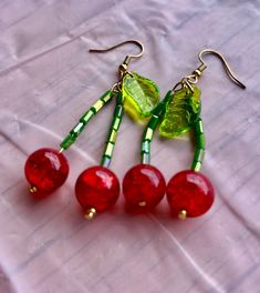 three red cherries with green leaves hang from gold - plated earwires