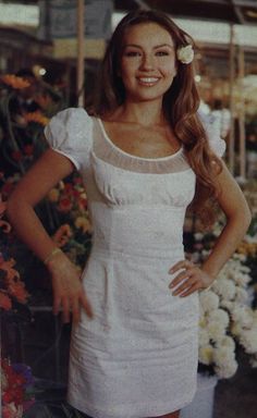 a woman standing in front of flowers with her hands on her hips and smiling at the camera