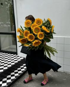 a woman walking down the street carrying a large bouquet of sunflowers