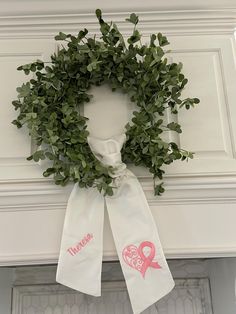 a white wreath with pink ribbon hanging on the wall