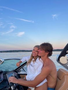 a man and woman sitting on the back of a boat in the water, with their arms around each other