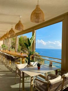 an outdoor dining area overlooking the ocean with wicker hanging from the ceiling and chairs