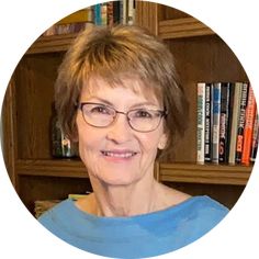 a woman with glasses is smiling in front of bookshelves and she's looking at the camera