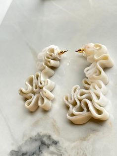 two pairs of white earrings sitting on top of a marble counter next to an orange object