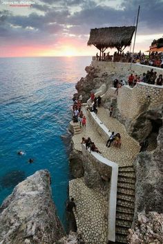 people are standing on the edge of a cliff overlooking the ocean at sunset or sunrise