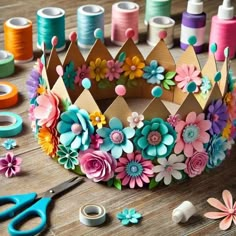 there is a crown made out of paper flowers and spools of thread on the table