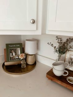 a white kitchen counter topped with a wooden tray and vase filled with flowers on top of it