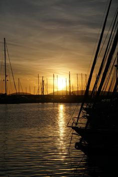 the sun is setting over some boats in the water