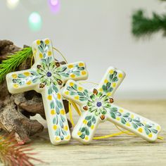 two ceramic cross ornaments sitting on top of a wooden table next to a pine tree