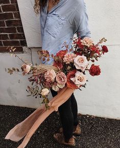 a woman holding a bouquet of flowers in front of a brick wall with her hands on the ground