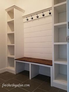 an empty white bench in the corner of a room with built - in shelving