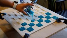 a person pouring blue liquid into a glass on top of a checkered tile table