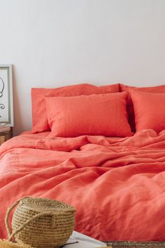 a bed with orange sheets and pillows in a room next to a basket on the floor