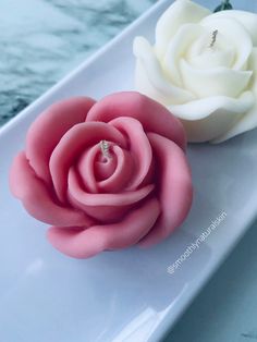 two fake flowers on a white plate next to each other, one pink and one white