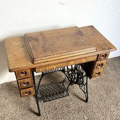 an old sewing machine sits on the floor next to a table with two drawers and a shelf