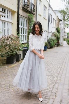 a woman is walking down the street wearing a white top and gray tulle skirt