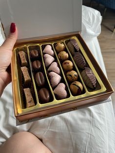 a woman holding a box full of chocolates on top of a white sheet covered bed