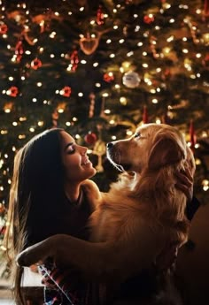 a woman sitting in front of a christmas tree with her dog looking up at it