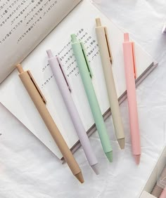 four different colored pens sitting next to each other on top of an open book,