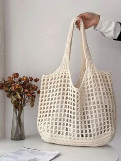 a hand holding a crocheted bag next to a vase with flowers in it