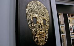 a gold beaded skull on a black wall next to a book shelf with books