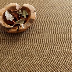 a wooden bowl filled with leaves on top of a brown carpet covered in woven material