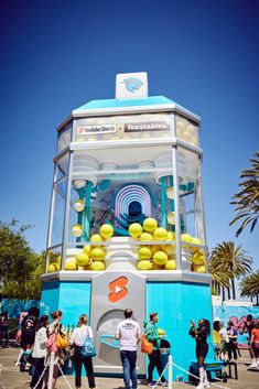 people standing around a blue and white machine with lemons on it's top