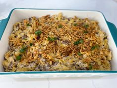 a casserole dish with meat, cheese and onions in a blue bowl on a white table