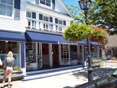 a woman walking down the sidewalk in front of a store with blue awnings