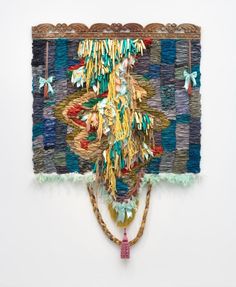 a piece of art made out of woven material and rope hanging on the wall with beads