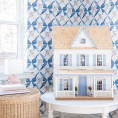 a doll house sitting on top of a white table next to a basket and window