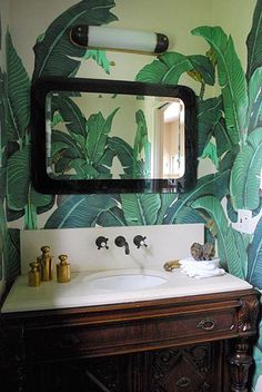 a bathroom with green wallpaper and a mirror above the sink, along with two gold faucets