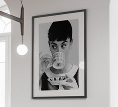 a black and white photo of a woman holding a coffee cup in front of her face