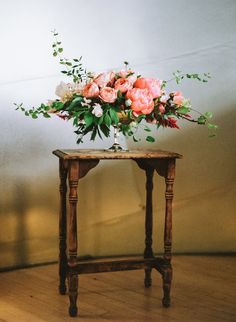 a small wooden table with flowers on it in front of a white wall and wood floor