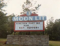 a sign that reads moon lit in front of some trees