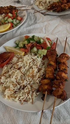 two plates filled with food and skewers on top of a white table cloth